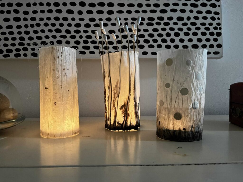 Drei selbstgemachte Kerzenschirme aus Butterbrotpapier mit Mohnkapseln, Konfetti und warmem LED-Licht.